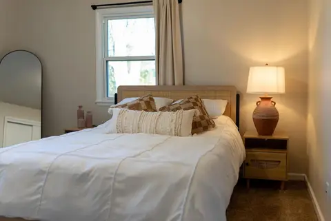 Queen bed with a woven headboard and a terracotta lamp by the window