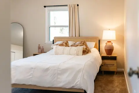 Queen bed with a rattan headboard, layered pillows, and a terracotta lamp