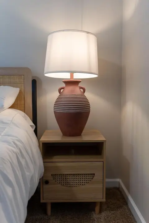 Terracotta table lamp on a wood nightstand beside the bed