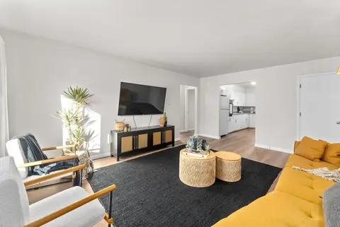Living room with a mustard sofa, an armchair, round woven tables, and a TV console