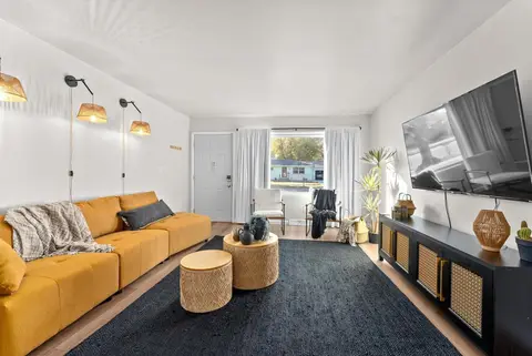 Living room with a mustard sofa, a navy rug, a wall-mounted TV, and woven wall sconces