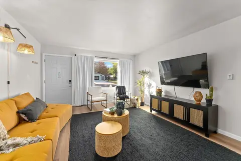 Mustard sofa, round side tables, and a wall-mounted TV over a black console