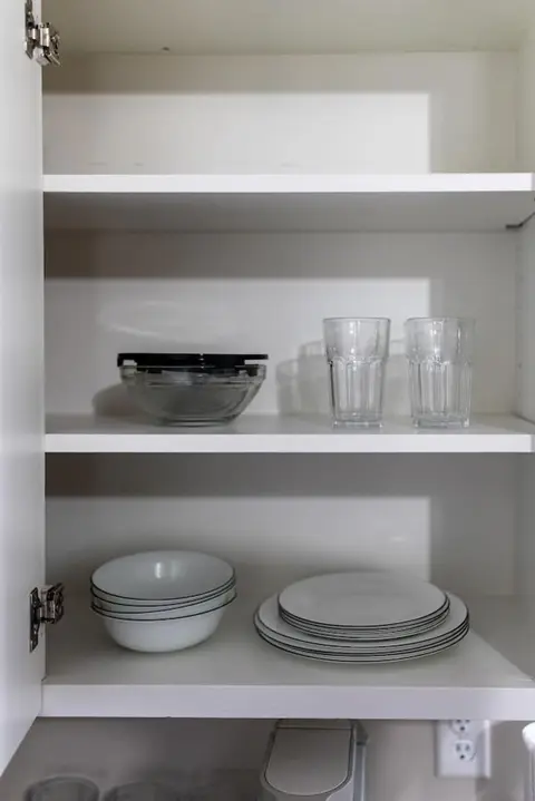 Glass tumblers and a mixing bowl on a cabinet shelf