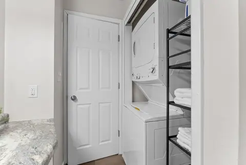 Stacked washer and dryer in a closet beside a shelf of folded towels
