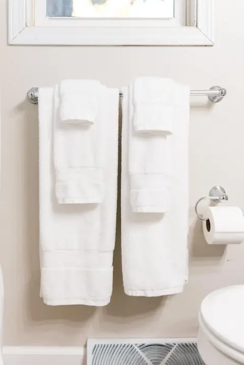 White towels on a bar beside a toilet paper holder