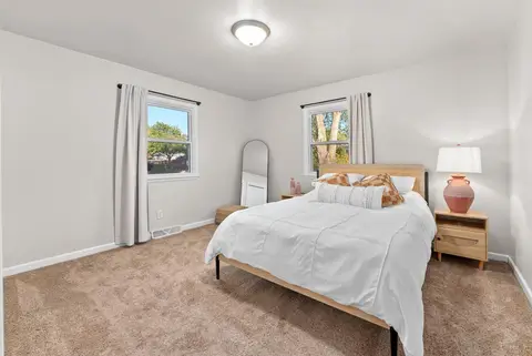 Queen bed with a rattan headboard between two windows, beside a floor mirror