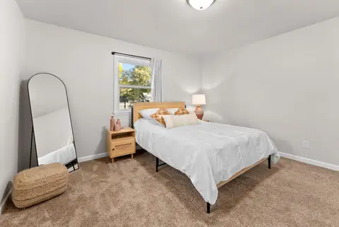 Queen bed with a light wood headboard, a woven pouf, and a floor mirror