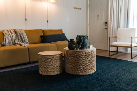 Mustard sofa with a throw blanket, woven side tables, and a white armchair