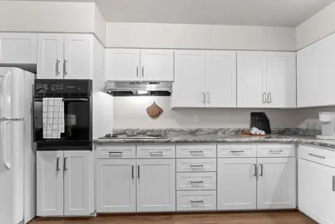 Kitchen wall with a black wall oven, a range hood, and white cabinets