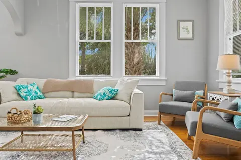 Cream sofa with teal pillows and two armchairs by tall windows