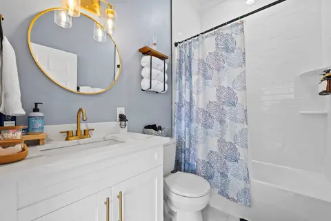 Bathroom with a white vanity, a round gold mirror, and a tub with a shower curtain