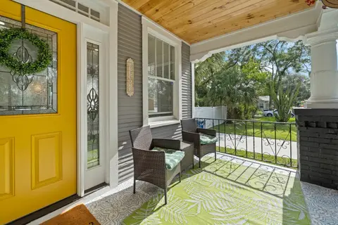 Covered front porch with two wicker chairs beside the yellow front door