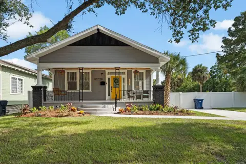 Front of the gray bungalow, with a porch swing, a yellow door, and front steps