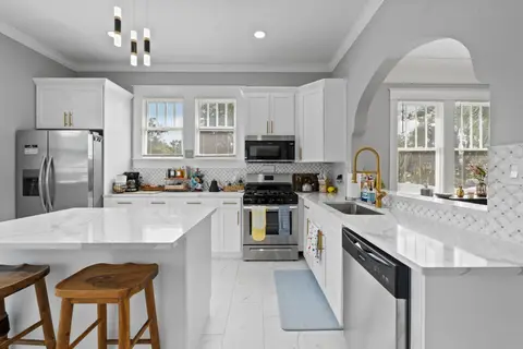 White kitchen with stainless appliances, a gas range, and island stools