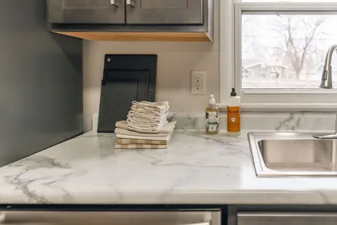 Kitchen sink and marble-look counter with folded towels and dish soap