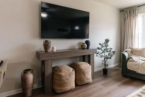 Wall-mounted TV above a wood console with woven poufs and vases