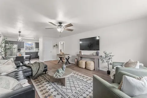 Open living room with a black leather sectional, a round coffee table, a TV, and the kitchen beyond