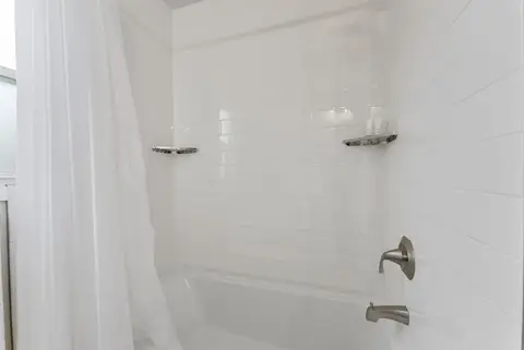 Tub and shower with a white curtain and a wall shelf