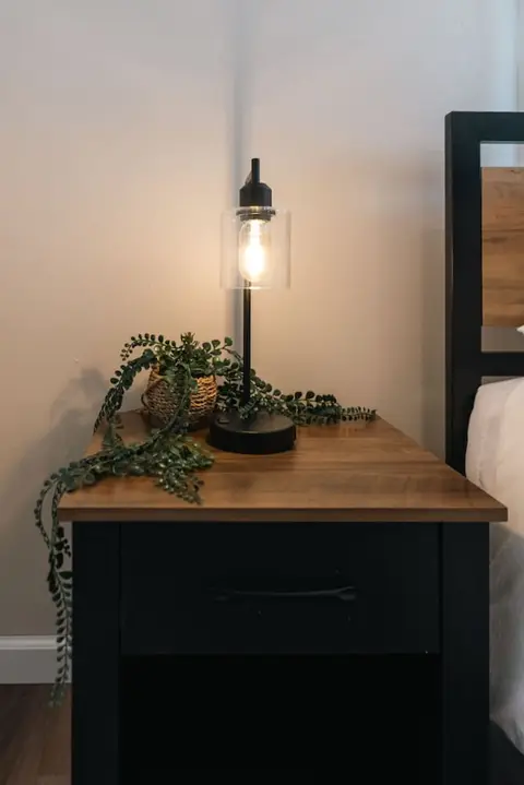 Bedside lamp and a trailing plant on a wood nightstand