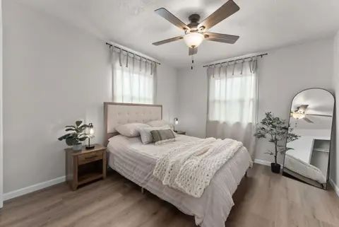 Bedroom with a queen bed, an upholstered headboard, an arched floor mirror, and a plant