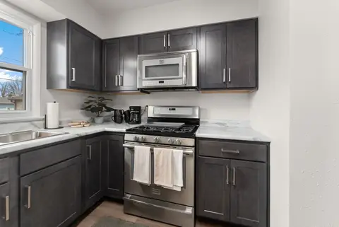Gas range under a microwave, with dark cabinets and a window over the sink