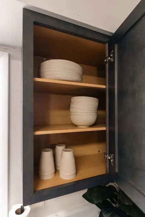 Open cabinet with stacked white bowls, plates, and cups