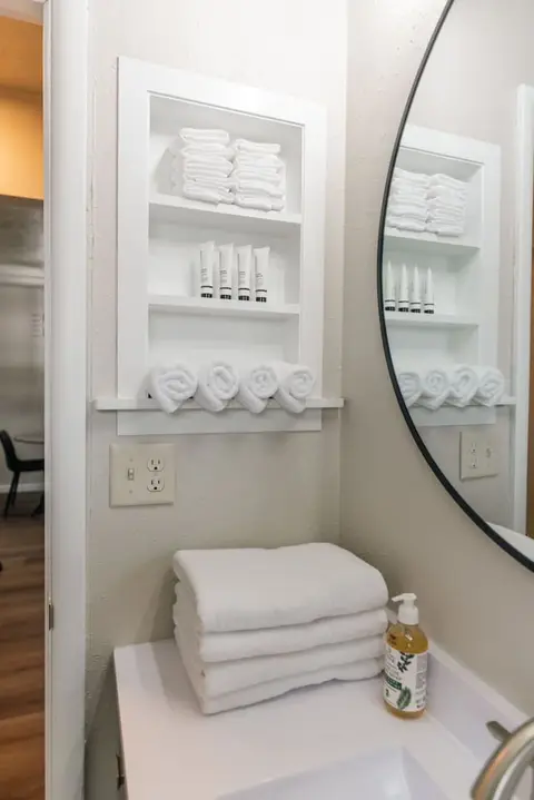 Rolled towels and toiletries on white shelves beside the bathroom mirror