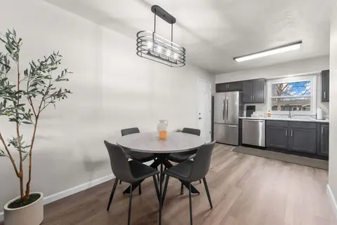 Round dining table with four chairs under a black pendant light, with the kitchen beyond
