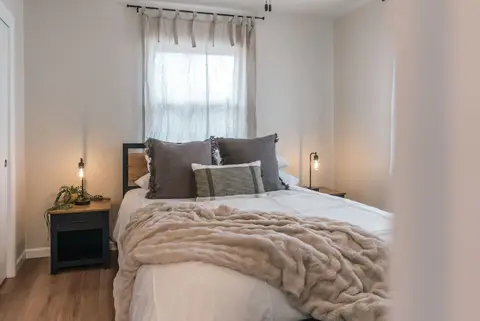 Queen bed with gray pillows and a knit throw, and a lamp on a dark nightstand