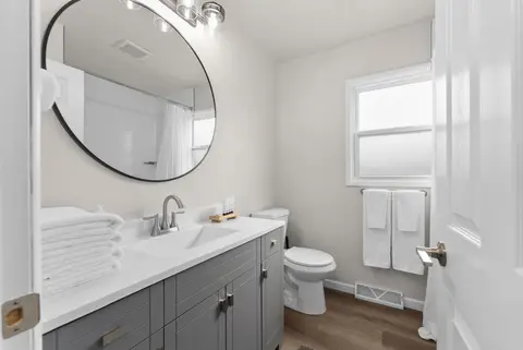 Bathroom with a round mirror, a dark vanity, a toilet, and white towels