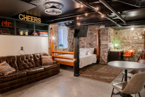 Studio with a leather Chesterfield, a four-poster queen bed, and stone walls under string lights