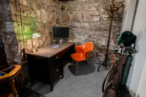 Desk corner with a coat rack and a vintage golf bag beside the stone wall