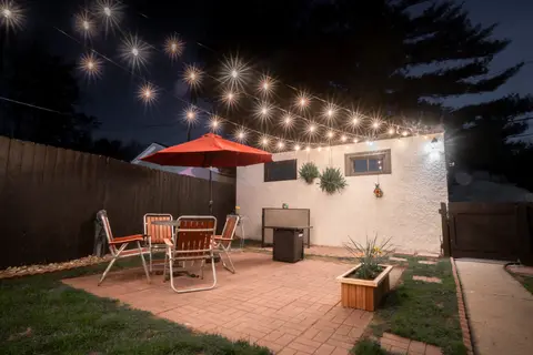 Shared backyard patio at night under string lights, with a red umbrella and table