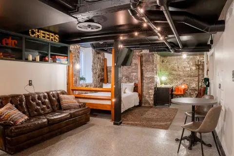 Studio with a tufted leather Chesterfield, a four-poster queen bed, and a café table under an open black ceiling