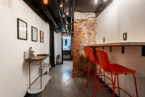 Red bar stools at a wall counter, a brass bar cart, and framed prints along the hall