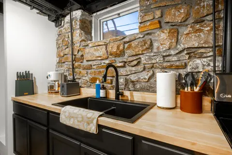 Black sink on a butcher block counter, below a stone wall and a basement window
