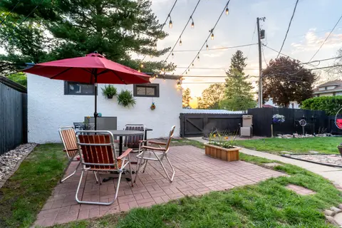 Brick patio with a red umbrella and vintage lawn chairs, inside a dark wood fence