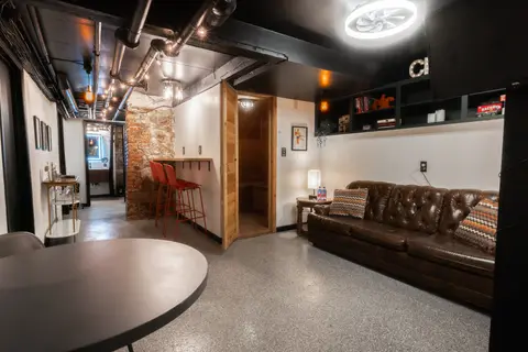 Studio looking toward the red bar stools and the wood-paneled sauna door, with the leather sofa on the right