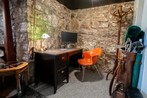 Desk and orange chair in a stone-walled corner, with a coat rack and golf bag