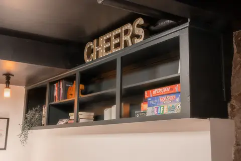 Shelf of board games and books under a lit CHEERS sign