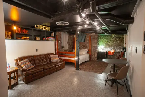 Leather sofa, four-poster bed, and café table, with a lit shelf of games above