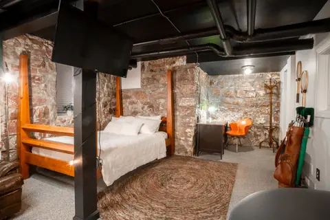 Four-poster queen bed against the stone walls, with a vintage golf bag and coat rack
