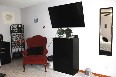 Sitting nook with a red wingback chair, a dresser, and a wall-mounted TV