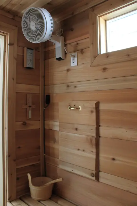 Sauna corner with a wall fan, a window, and a wooden bucket