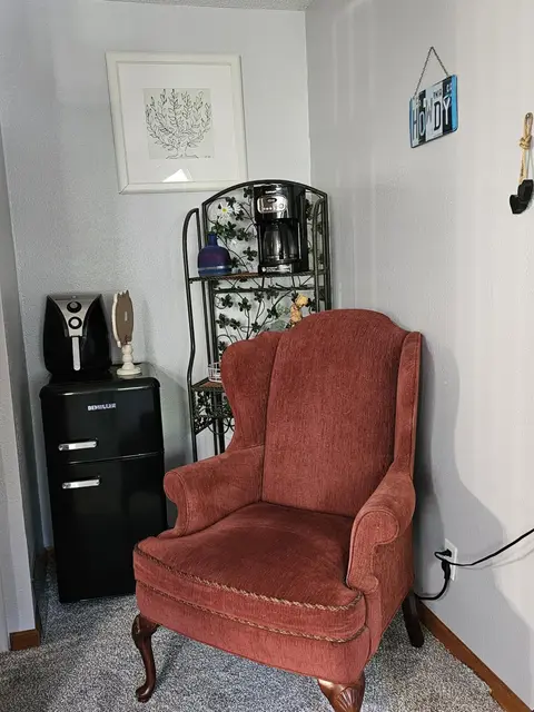 Wingback chair beside a mini fridge, an air fryer, and a coffee maker on a rack