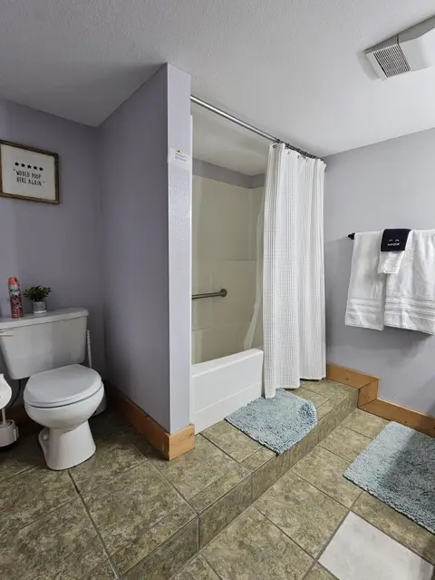 Bathroom with a toilet, a grab bar, and a tub and shower