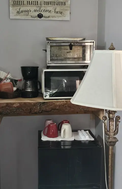 Coffee station with a coffee maker, microwave, toaster oven, mugs, and a mini fridge