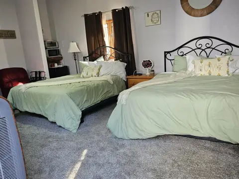Two queen beds side by side, with a lamp and a coffee station beyond