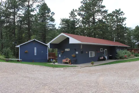 Small blue cabin beside the long main building and a gravel drive