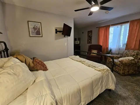 Queen bed with a cream comforter, an armchair, and orange curtains